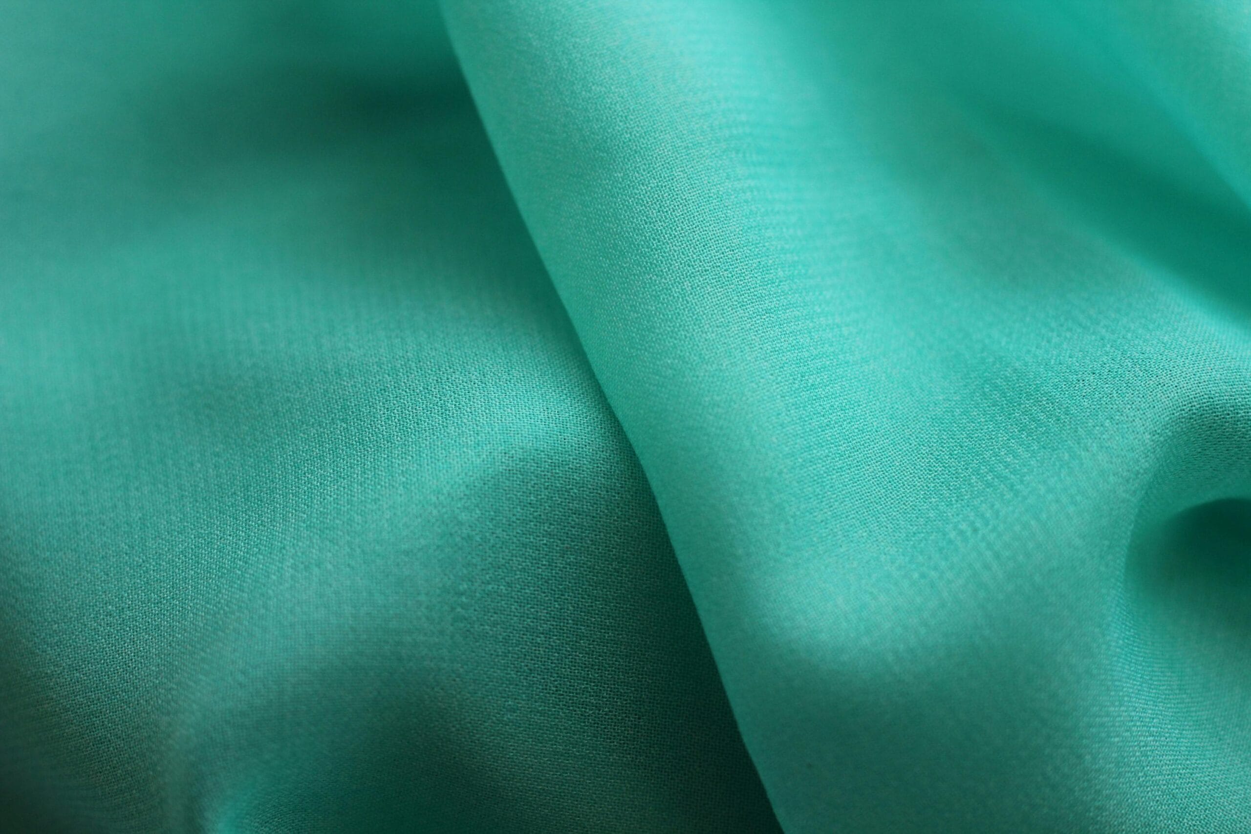 Close-up of soft teal fabric with flowing folds, highlighting the rich, blue-green tone that makes teal a standout wardrobe colour